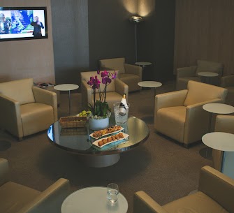 A spotless general aviation terminal lounge cleaned by Fort Worth Cleaning Professionals, featuring comfortable armchairs, a gleaming glass table, and a vase of three vibrant purple tulips, showcasing pristine condition and attention to detail.