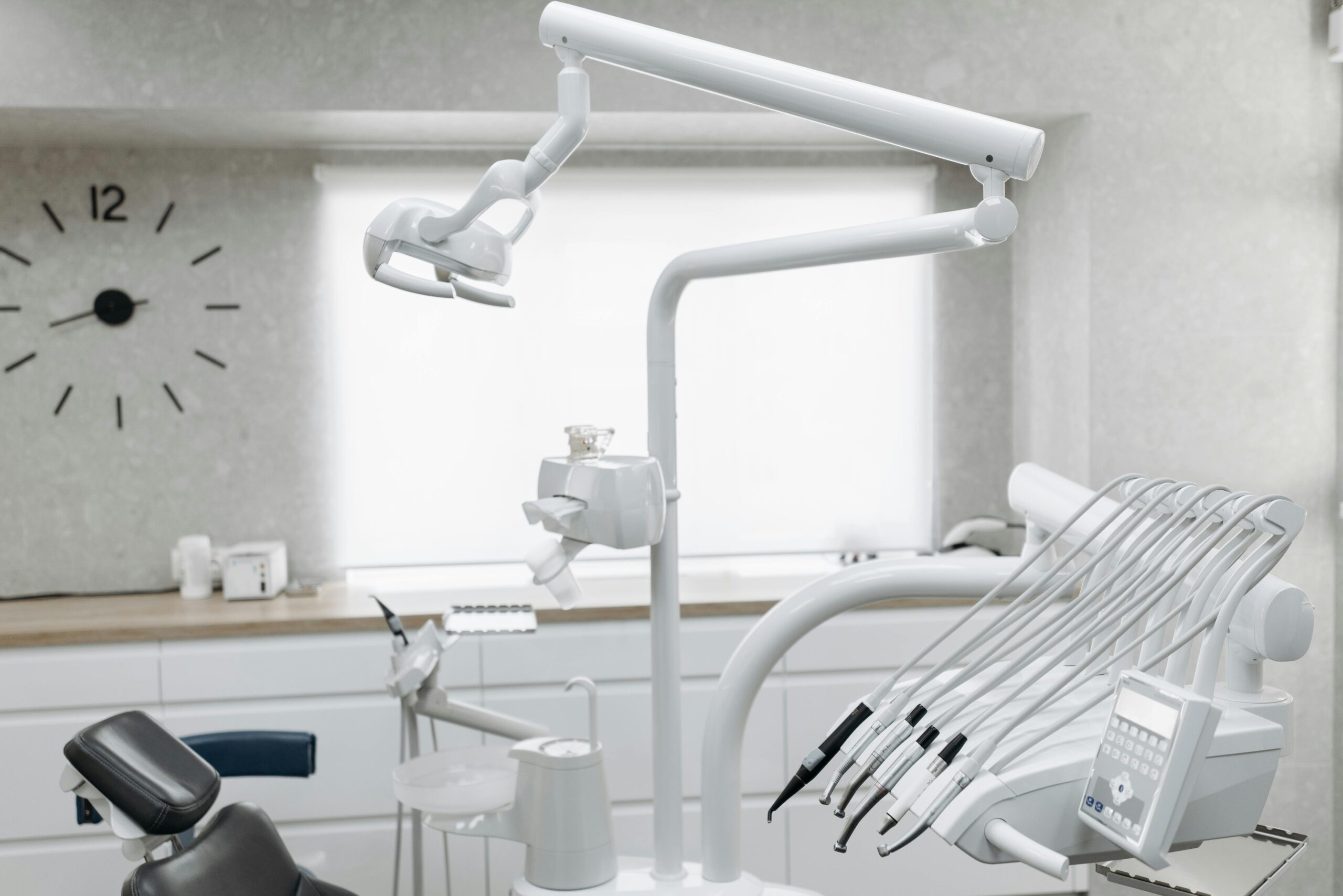 A clean, modern dental office with bright lighting. The reception area features comfortable seating and a sleek desk. The treatment room has a dental chair, neatly organized tools, and spotless surfaces, emphasizing a sterile and welcoming environment.